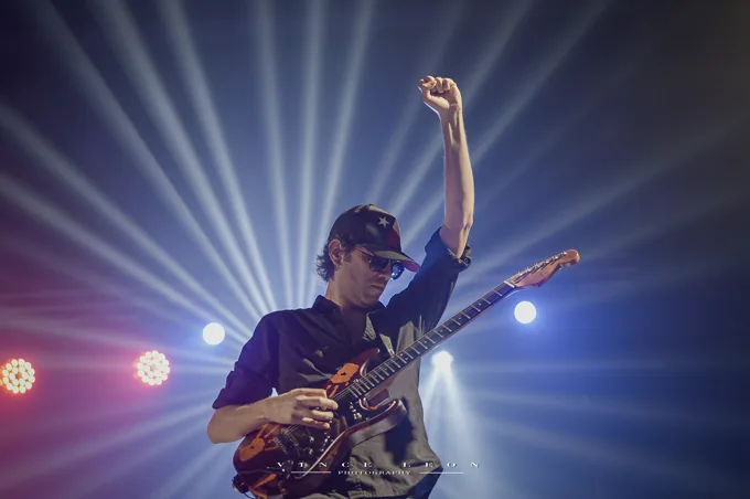 Guitarist raising a fist beneath white stage lights