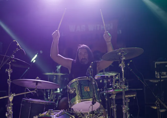 Drummer raising both sticks under purple lights