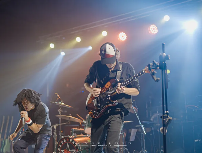 Vocalist and guitarist under white stage beams